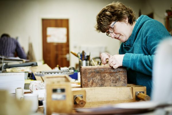 A woman working at a bench on the binding of a book in need of restoration.