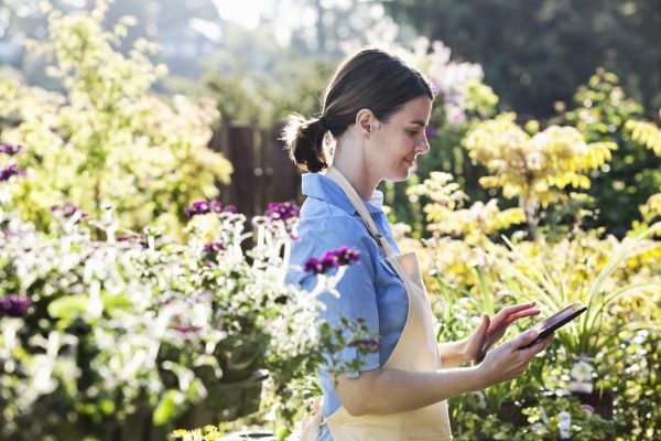 Caucasian woman employee of a garden center nursery texting in an order for new plants.